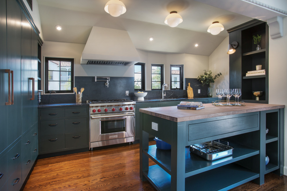 Mid-sized mediterranean l-shaped eat-in kitchen in Los Angeles with an undermount sink, flat-panel cabinets, green cabinets, wood benchtops, green splashback, engineered quartz splashback, stainless steel appliances, medium hardwood floors, with island, brown floor, green benchtop and vaulted.