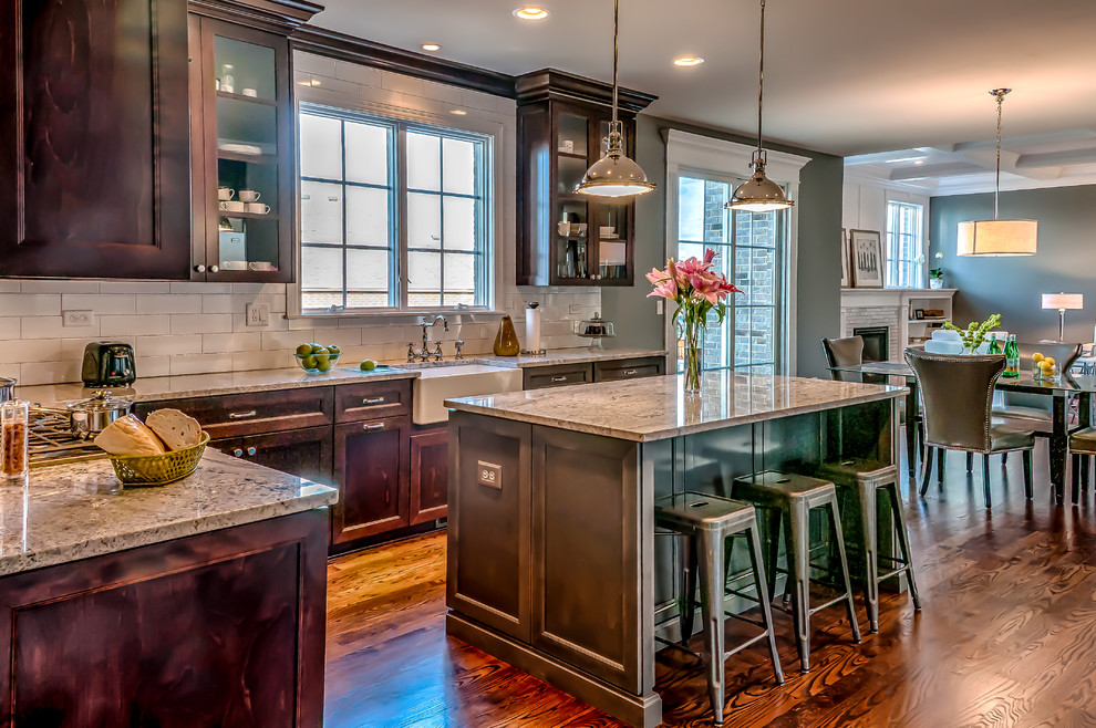Example of a mid-sized transitional u-shaped dark wood floor eat-in kitchen design in Chicago with a farmhouse sink, recessed-panel cabinets, medium tone wood cabinets, granite countertops, white backsplash, subway tile backsplash, stainless steel appliances and an island