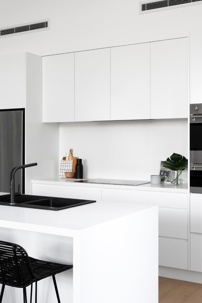 Design ideas for a contemporary galley kitchen in Melbourne with a drop-in sink, flat-panel cabinets, white cabinets, stainless steel appliances, medium hardwood floors, with island, brown floor and white benchtop.