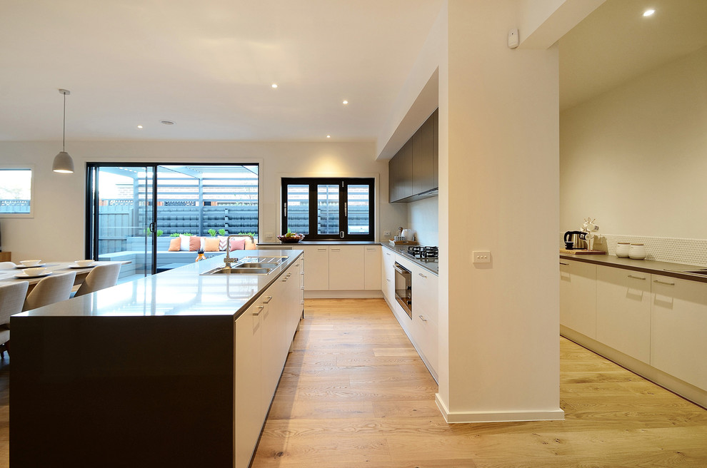 Photo of a large contemporary l-shaped eat-in kitchen in Melbourne with a double-bowl sink, quartz benchtops, white splashback, cement tile splashback, stainless steel appliances, medium hardwood floors and with island.