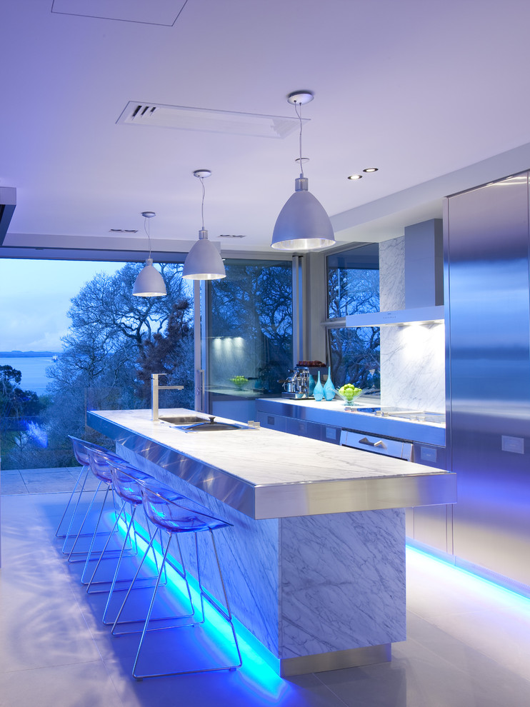 Photo of a large contemporary galley eat-in kitchen in Los Angeles with stainless steel appliances, flat-panel cabinets, stainless steel cabinets, white splashback, stainless steel benchtops, marble splashback and with island.