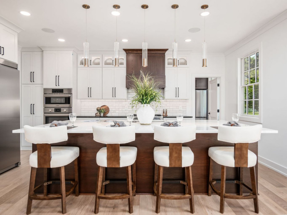 Large transitional l-shaped light wood floor and brown floor eat-in kitchen photo in Columbus with an undermount sink, flat-panel cabinets, white cabinets, quartz countertops, white backsplash, subway tile backsplash, stainless steel appliances, an island and black countertops