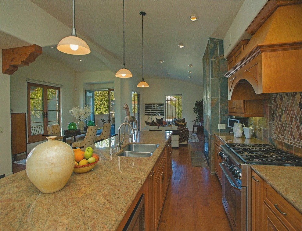 This is an example of a mid-sized mediterranean galley open plan kitchen in Santa Barbara with an undermount sink, raised-panel cabinets, medium wood cabinets, granite benchtops, multi-coloured splashback, stone tile splashback, stainless steel appliances, medium hardwood floors and with island.