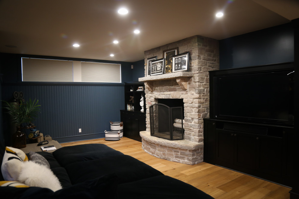 Aménagement d'un grand sous-sol classique enterré avec un bar de salon, un mur bleu, parquet clair, une cheminée standard et un manteau de cheminée en pierre.