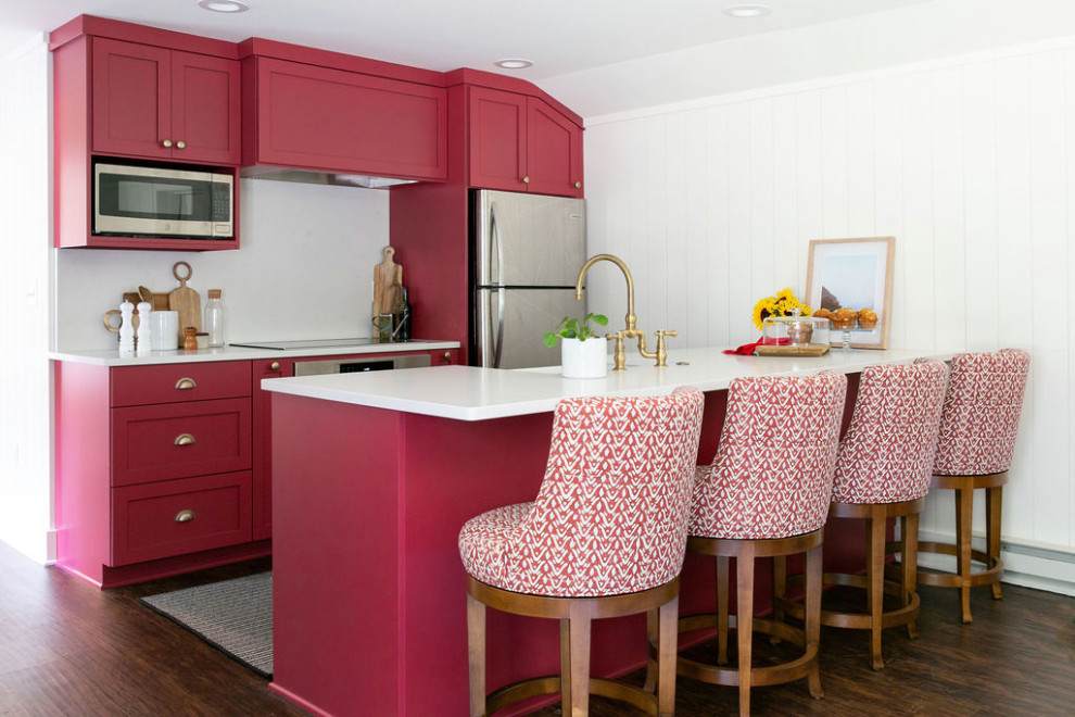 Small beach style galley kitchen in New York with a farmhouse sink, shaker cabinets, red cabinets, quartz benchtops, white splashback, engineered quartz splashback, stainless steel appliances, vinyl floors, a peninsula, brown floor and brown benchtop.