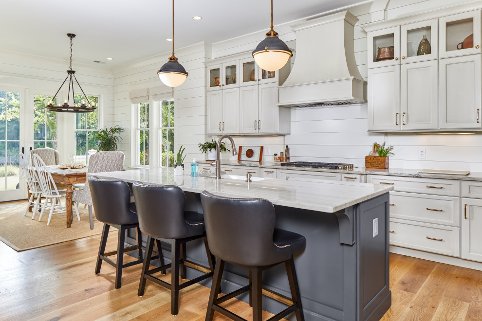 Eat-in kitchen - large transitional brown floor and medium tone wood floor eat-in kitchen idea with a farmhouse sink, granite countertops, white backsplash, wood backsplash, an island, white countertops, shaker cabinets and white cabinets