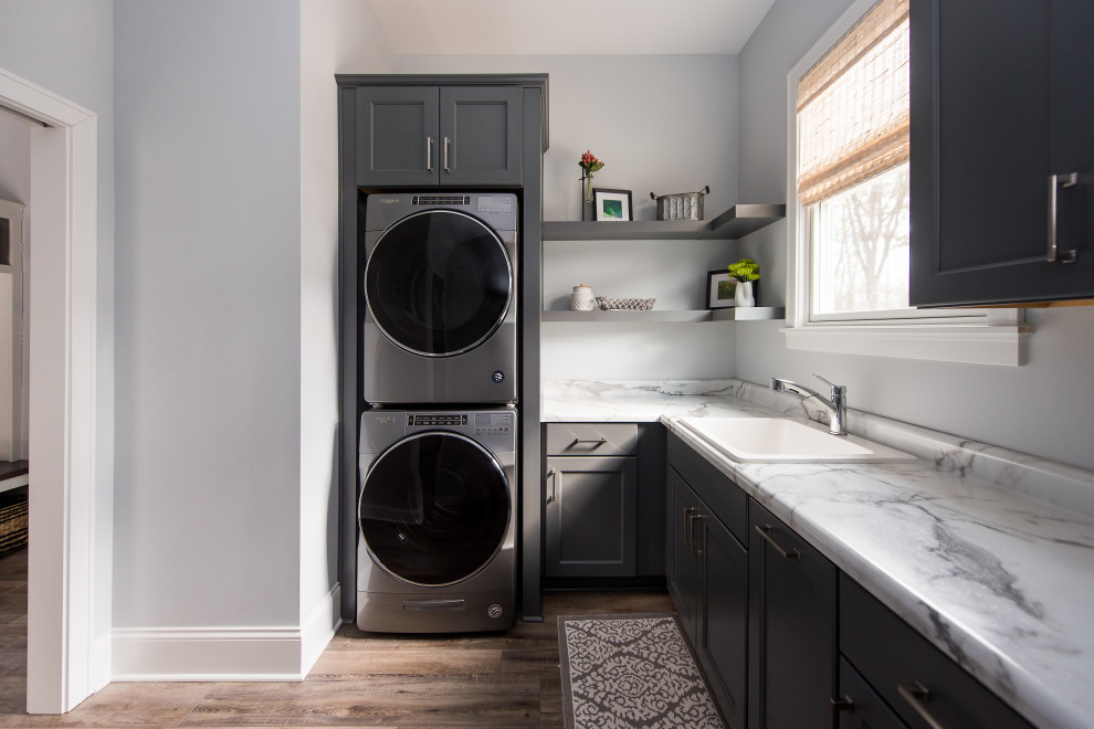 Design ideas for a mid-sized transitional l-shaped dedicated laundry room in Indianapolis with an undermount sink, shaker cabinets, grey cabinets, marble benchtops, beige walls, dark hardwood floors and a stacked washer and dryer.