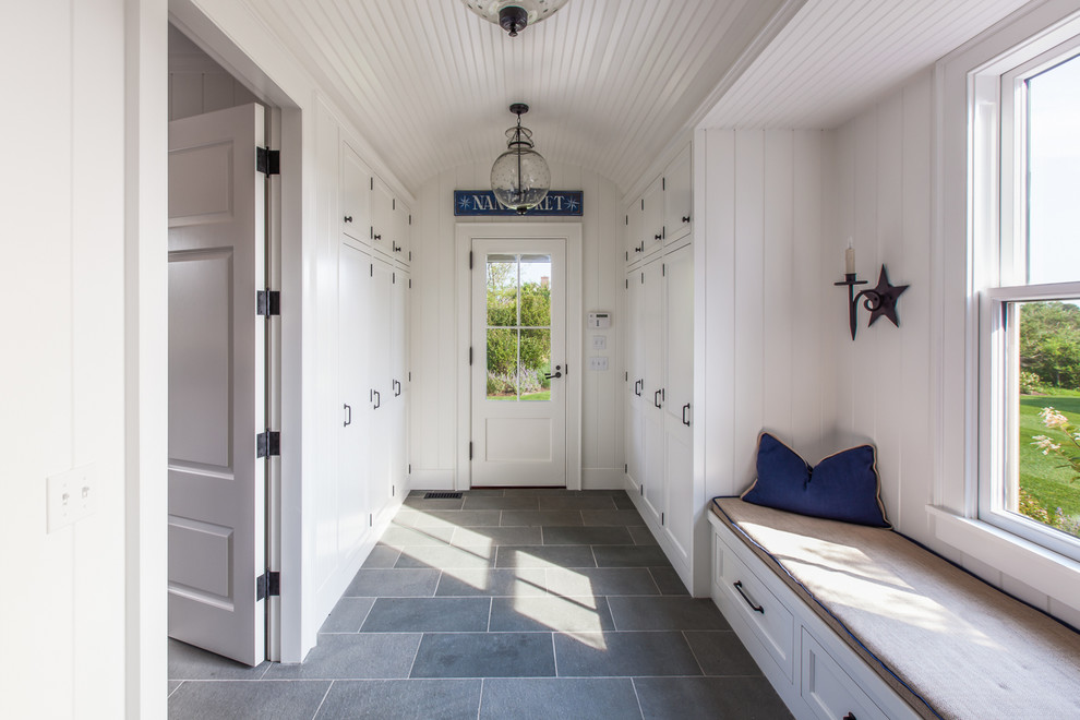 Photo of a large beach style mudroom in Boston with white walls, a single front door, a glass front door and grey floor.