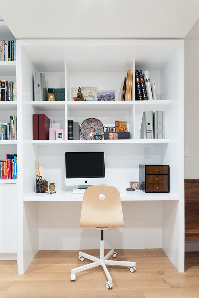 This is an example of a small transitional study room in New York with white walls, medium hardwood floors, a built-in desk and brown floor.