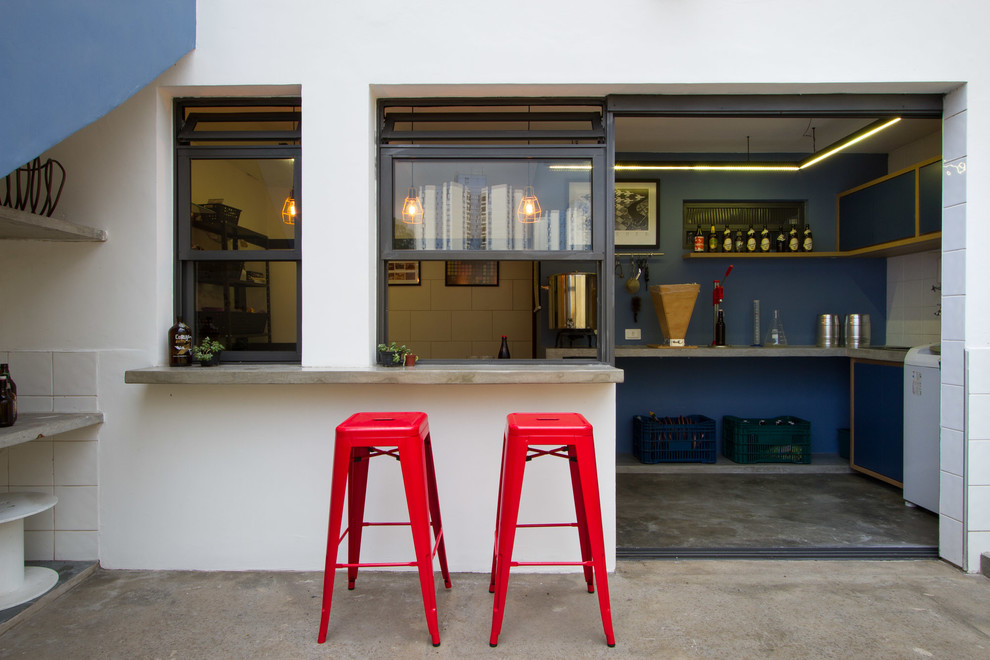 This is an example of a mid-sized industrial l-shaped seated home bar in Other with a drop-in sink, flat-panel cabinets, blue cabinets, concrete benchtops, blue splashback, concrete floors, grey floor and grey benchtop.