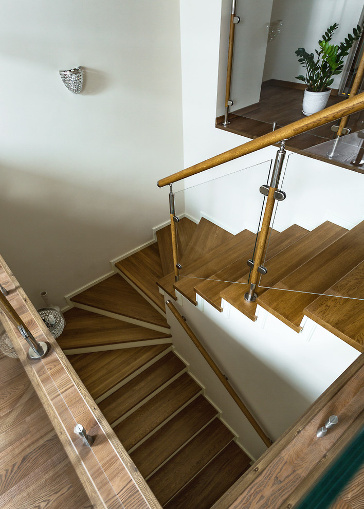 На фото: изогнутая лестница с деревянными ступенями и перилами из смешанных материалов с