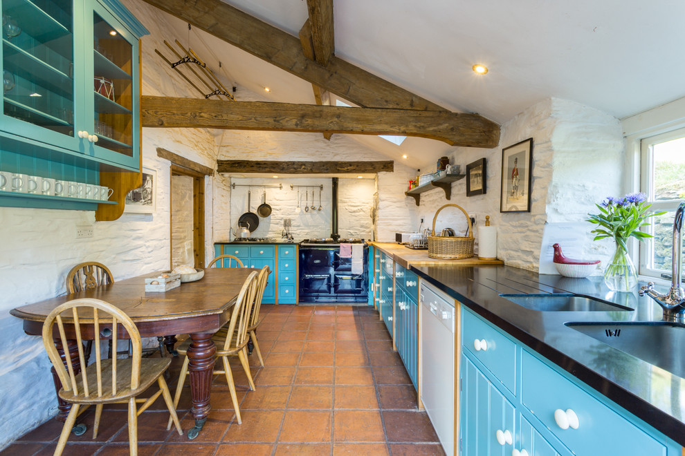 Design ideas for a mid-sized country l-shaped eat-in kitchen in Cardiff with an undermount sink, flat-panel cabinets, blue cabinets, window splashback, coloured appliances, terra-cotta floors, with island, brown floor and multi-coloured benchtop.