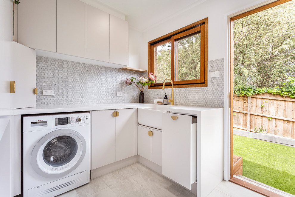 Inspiration for a mid-sized contemporary l-shaped laundry room in Melbourne with a farmhouse sink, flat-panel cabinets, quartz benchtops, white walls, porcelain floors, a side-by-side washer and dryer, grey floor, white benchtop and beige cabinets.