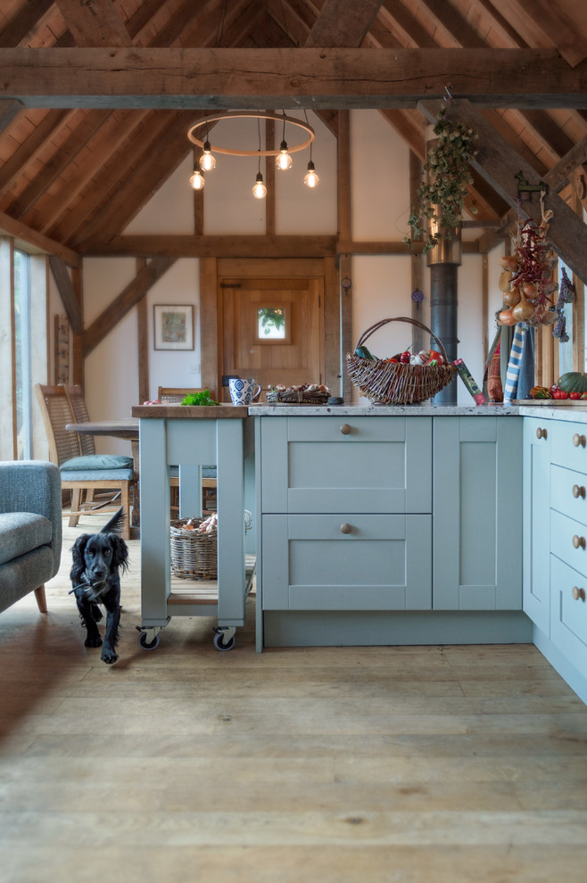 Mid-sized country u-shaped eat-in kitchen in Cornwall with a farmhouse sink, shaker cabinets, green cabinets, granite benchtops, white splashback, stainless steel appliances, medium hardwood floors, with island, beige floor and white benchtop.