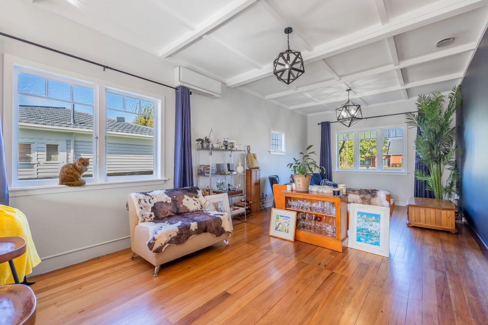 Photo of a large eclectic open concept living room in Auckland with medium hardwood floors, brown floor and coffered.