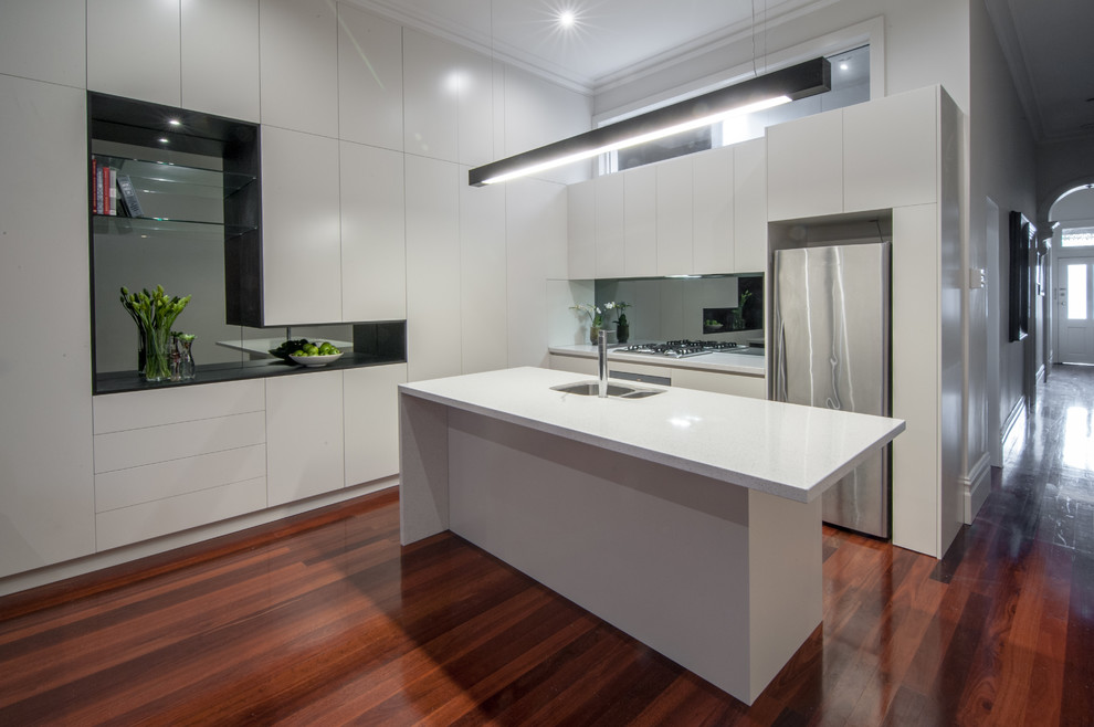 Design ideas for a small contemporary l-shaped eat-in kitchen in Melbourne with an undermount sink, flat-panel cabinets, white cabinets, quartz benchtops, metallic splashback, glass sheet splashback, stainless steel appliances, medium hardwood floors and with island.