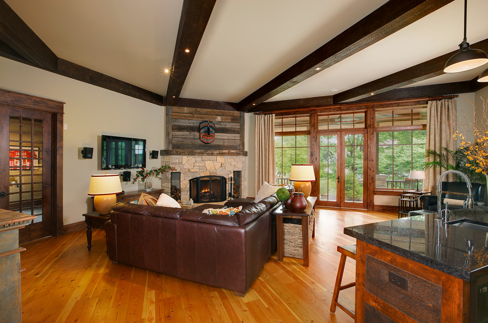 This is an example of a mid-sized arts and crafts open concept family room in Chicago with a home bar, beige walls, medium hardwood floors, a standard fireplace, a stone fireplace surround and a wall-mounted tv.