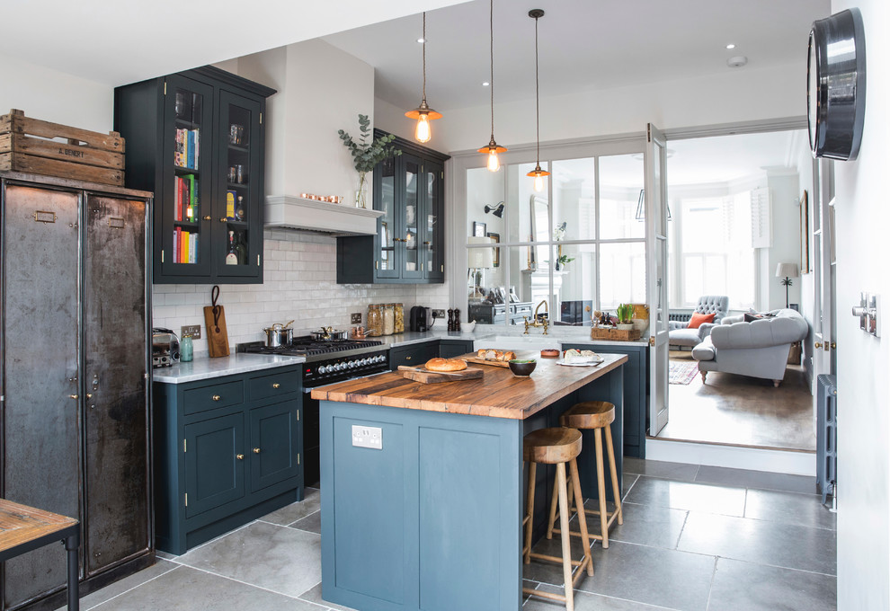 Photo of a mid-sized transitional l-shaped eat-in kitchen in London with a farmhouse sink, shaker cabinets, wood benchtops, limestone floors, with island, blue cabinets, grey floor, white splashback and subway tile splashback.