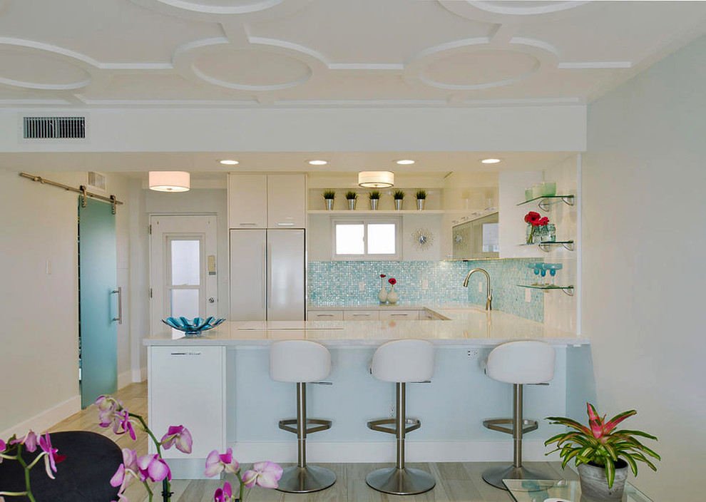 Design ideas for a transitional u-shaped eat-in kitchen in Tampa with an undermount sink, flat-panel cabinets, white cabinets, glass benchtops, blue splashback, glass tile splashback, white appliances, light hardwood floors and no island.
