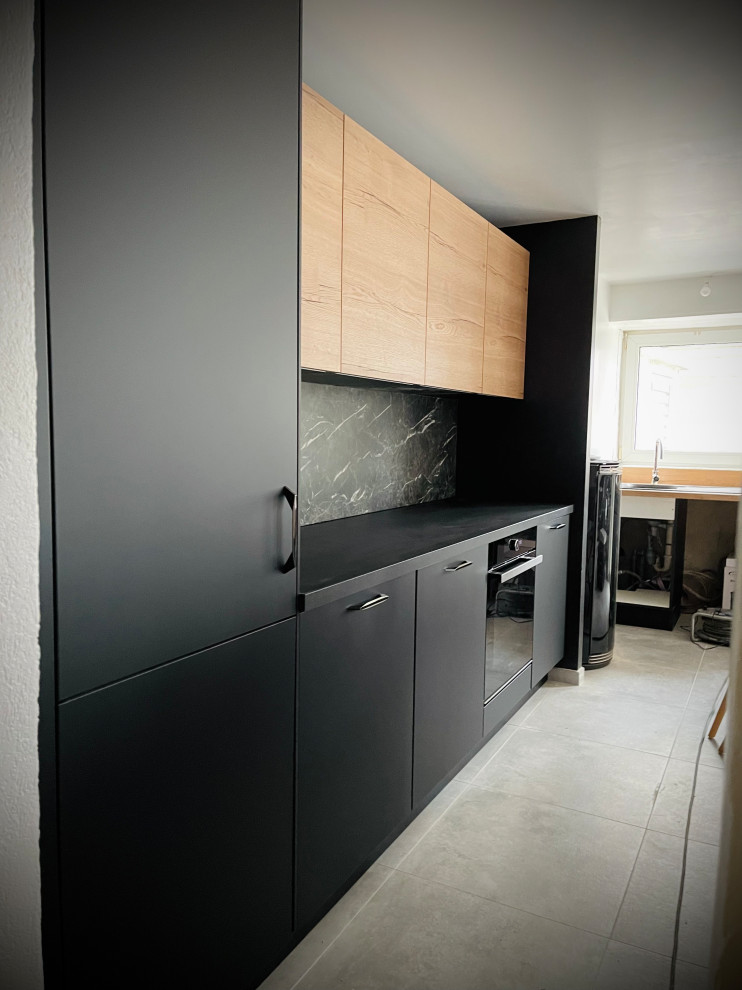 This is an example of a large contemporary galley open plan kitchen with an undermount sink, black cabinets, laminate benchtops, black splashback, marble splashback, panelled appliances, ceramic floors, with island, grey floor and black benchtop.