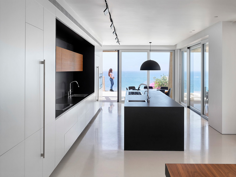 Inspiration for a modern galley open plan kitchen in Tel Aviv with an undermount sink, flat-panel cabinets, white cabinets, black splashback, panelled appliances, with island and white floor.