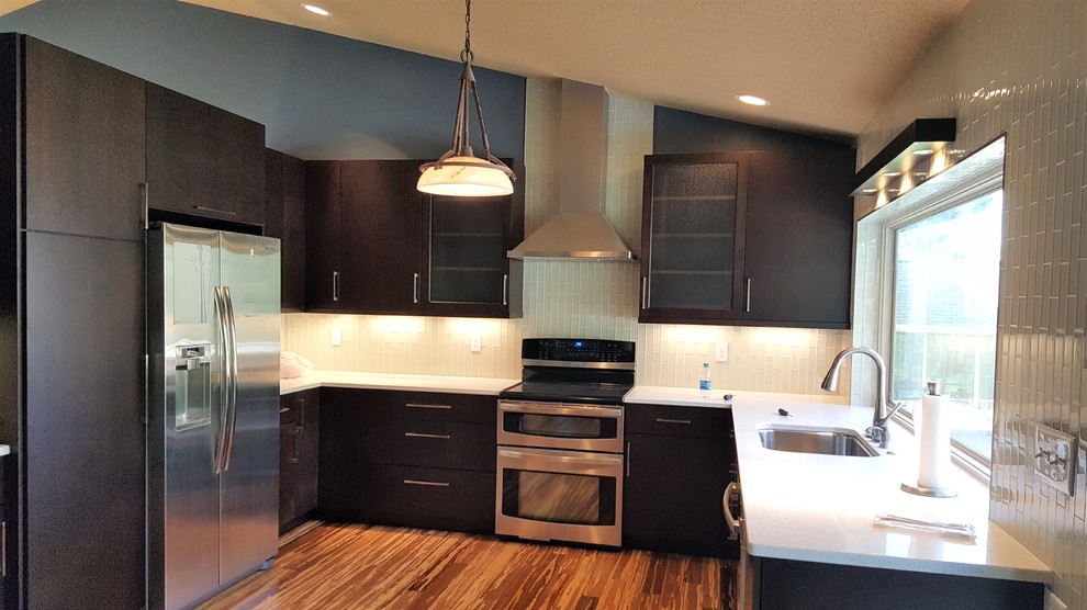 Photo of a mid-sized contemporary u-shaped eat-in kitchen in Cedar Rapids with an undermount sink, flat-panel cabinets, black cabinets, quartz benchtops, grey splashback, glass tile splashback, stainless steel appliances, bamboo floors and multi-coloured floor.