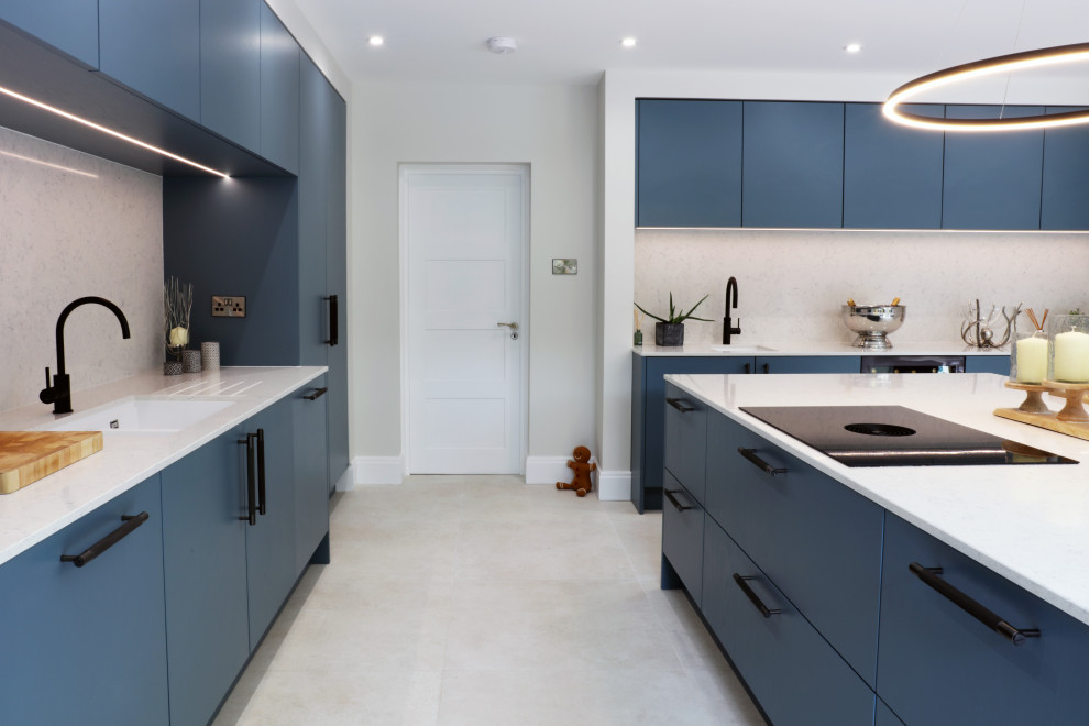 This is an example of a large modern open plan kitchen in West Midlands with a single-bowl sink, flat-panel cabinets, blue cabinets, quartzite benchtops, white splashback, engineered quartz splashback, black appliances, porcelain floors, beige floor and white benchtop.
