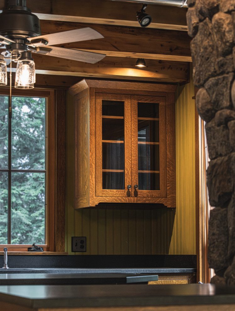 Mountain style medium tone wood floor and exposed beam kitchen photo with an undermount sink, shaker cabinets, granite countertops, black backsplash, granite backsplash, stainless steel appliances, an island and black countertops