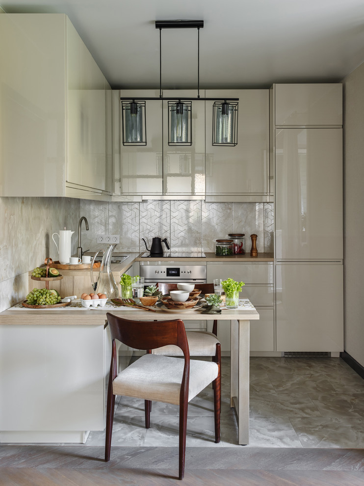 This is an example of a contemporary l-shaped kitchen in Moscow with flat-panel cabinets, beige cabinets, stainless steel appliances, no island, grey floor and beige benchtop.