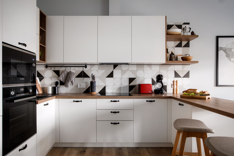 Design ideas for a scandinavian u-shaped kitchen in Yekaterinburg with flat-panel cabinets, white cabinets, wood benchtops, multi-coloured splashback, black appliances, light hardwood floors and a peninsula.