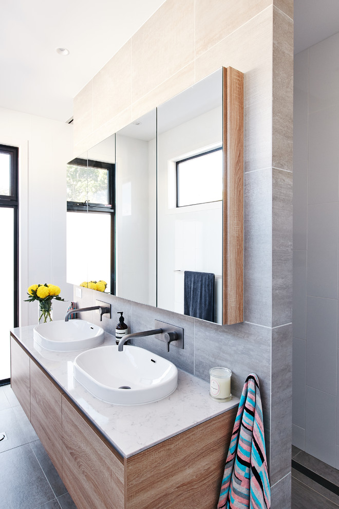 This is an example of a large contemporary master bathroom in Melbourne with flat-panel cabinets, light wood cabinets, a shower/bathtub combo, white tile, glass sheet wall, grey walls, ceramic floors, a drop-in sink, engineered quartz benchtops, grey floor, an open shower and white benchtops.