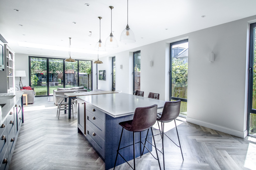 Photo of a large contemporary l-shaped open plan kitchen in Surrey with an undermount sink, shaker cabinets, blue cabinets, solid surface benchtops, white splashback, mosaic tile splashback, stainless steel appliances, medium hardwood floors, with island, grey floor and white benchtop.