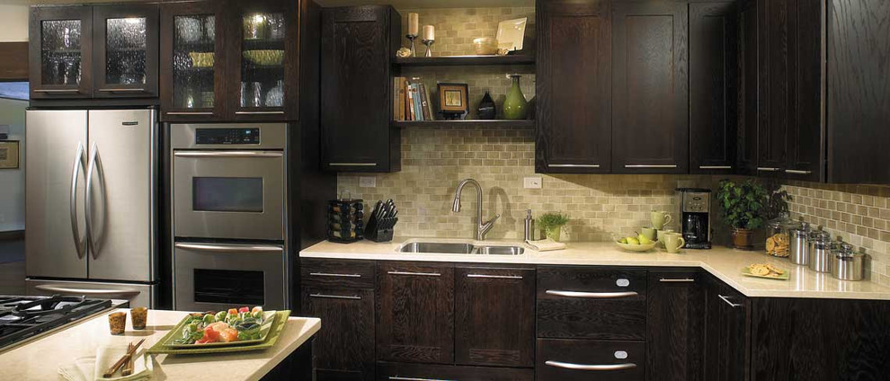 Enclosed kitchen - large transitional l-shaped enclosed kitchen idea with an undermount sink, shaker cabinets, dark wood cabinets, granite countertops, beige backsplash, stone tile backsplash, stainless steel appliances and an island