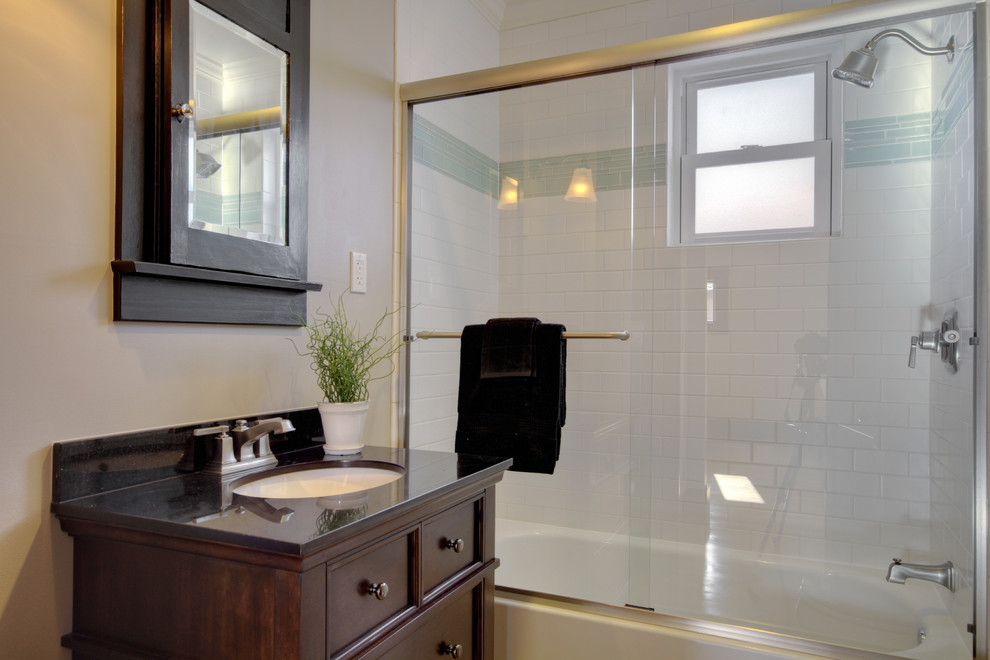 This is an example of a mid-sized eclectic bathroom in Denver with recessed-panel cabinets, dark wood cabinets, a shower/bathtub combo, white tile, subway tile, an undermount sink and a sliding shower screen.