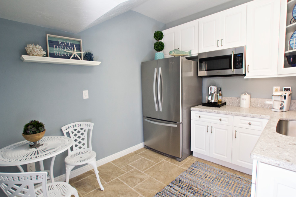 Small beach style l-shaped eat-in kitchen in San Diego with a drop-in sink, raised-panel cabinets, white cabinets, quartz benchtops, beige splashback, stone slab splashback, stainless steel appliances, ceramic floors, no island, beige floor and beige benchtop.