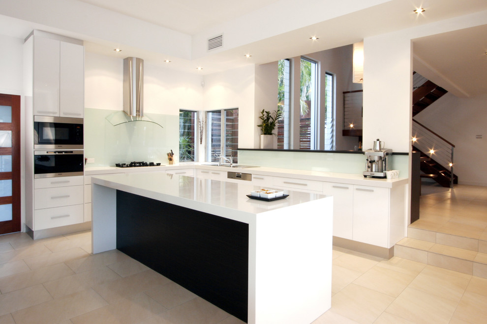 This is an example of a contemporary l-shaped kitchen in Brisbane with flat-panel cabinets, white cabinets, green splashback, glass sheet splashback and stainless steel appliances.