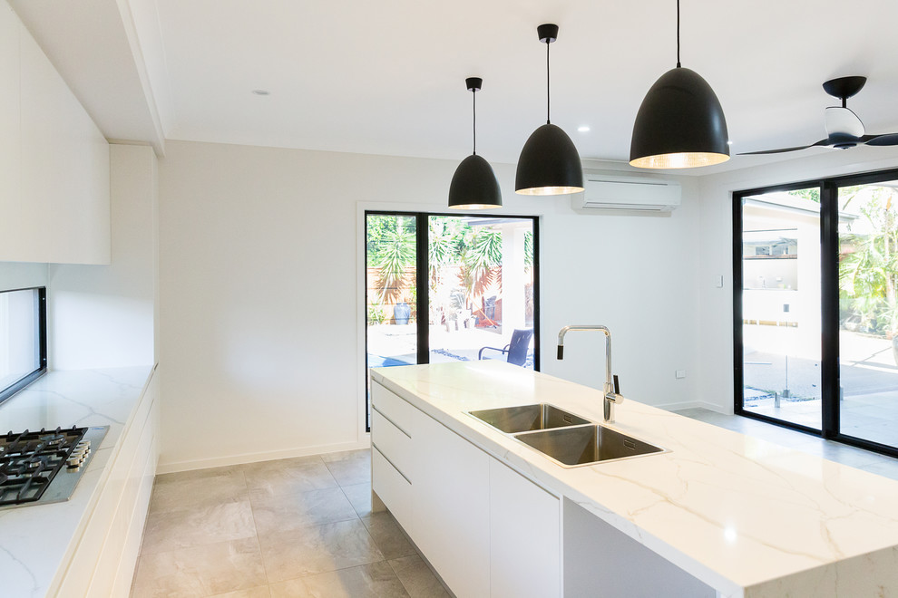 Contemporary galley open plan kitchen in Townsville with a double-bowl sink, flat-panel cabinets, white cabinets, marble benchtops, white splashback, glass sheet splashback, stainless steel appliances, ceramic floors, with island and grey floor.