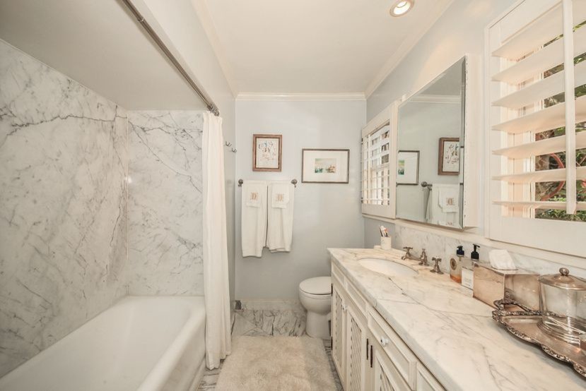 Mid-sized transitional 3/4 bathroom in Los Angeles with louvered cabinets, white cabinets, an alcove tub, a shower/bathtub combo, a two-piece toilet, white tile, marble, grey walls, marble floors, an undermount sink, marble benchtops, white floor and a shower curtain.