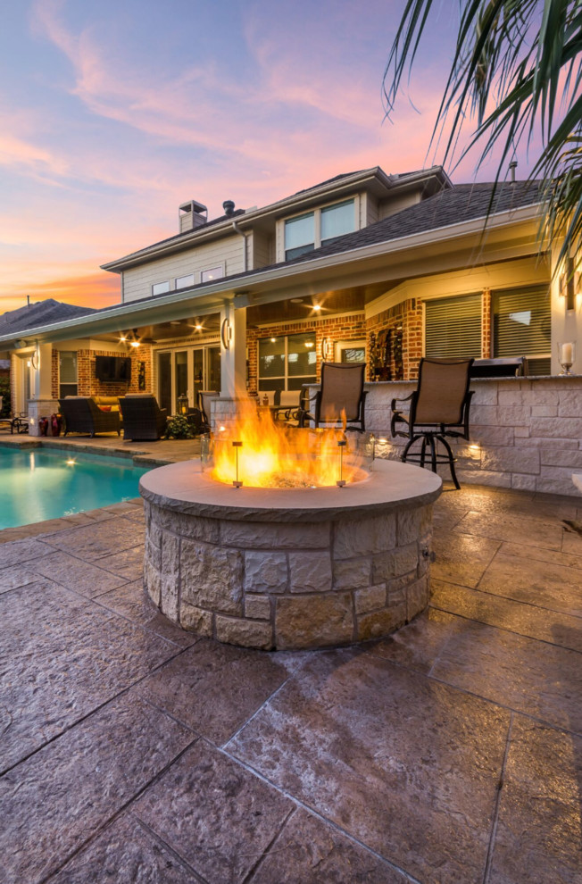 This is an example of a mid-sized traditional backyard patio in Dallas with stamped concrete, a roof extension and a fire feature.