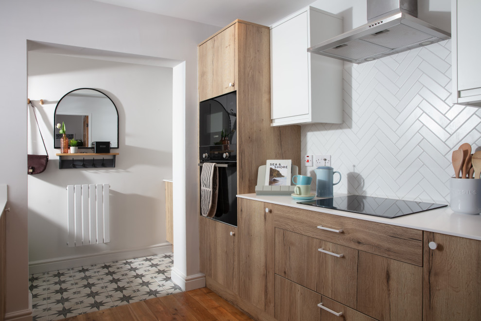 Inspiration for a small scandinavian galley separate kitchen in Cornwall with a single-bowl sink, flat-panel cabinets, medium wood cabinets, solid surface benchtops, white splashback, subway tile splashback, panelled appliances, medium hardwood floors, no island, brown floor and white benchtop.