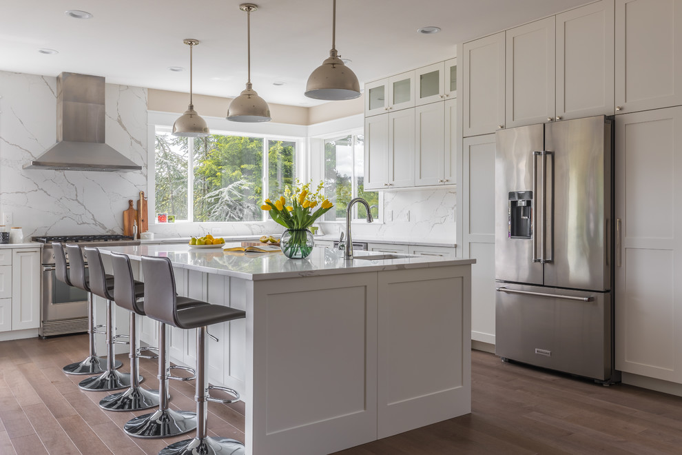 Inspiration for a large transitional l-shaped medium tone wood floor and brown floor kitchen remodel in Seattle with an undermount sink, shaker cabinets, white cabinets, granite countertops, white backsplash, stone slab backsplash, stainless steel appliances, an island and white countertops