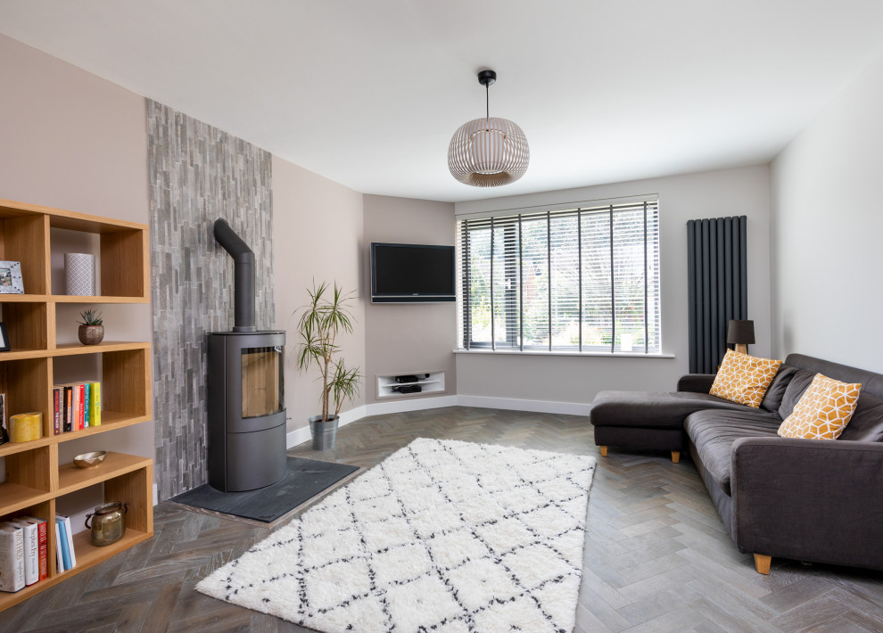 Inspiration pour un salon gris et blanc design de taille moyenne et fermé avec un mur gris, un sol en bois brun, un poêle à bois, un manteau de cheminée en carrelage, un sol gris et éclairage.