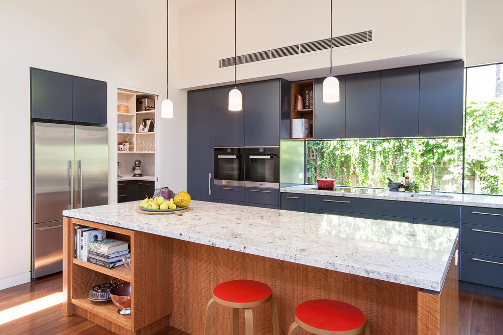 Inspiration for a large transitional single-wall open plan kitchen in Melbourne with a double-bowl sink, blue cabinets, granite benchtops, black appliances, medium hardwood floors, with island, white benchtop and window splashback.