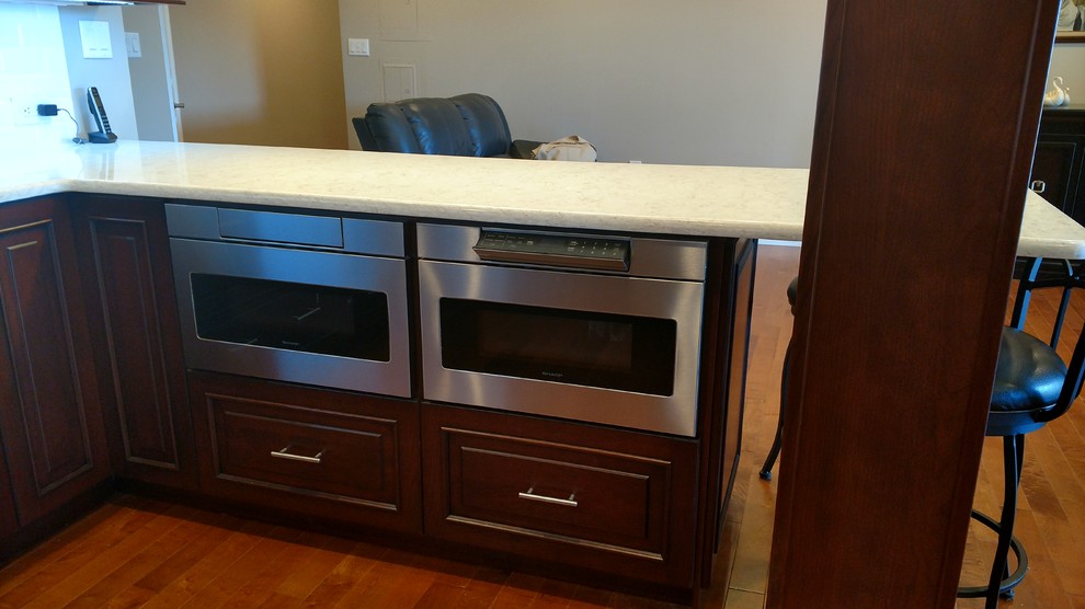 Example of a large transitional u-shaped medium tone wood floor kitchen design in New York with an undermount sink, raised-panel cabinets, dark wood cabinets, white backsplash, subway tile backsplash, stainless steel appliances and a peninsula