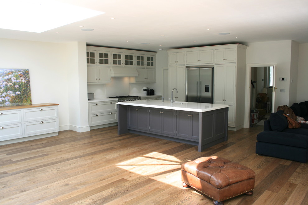 This is an example of a large transitional l-shaped eat-in kitchen in London with an undermount sink, quartz benchtops, stainless steel appliances, dark hardwood floors, with island, beaded inset cabinets and grey cabinets.