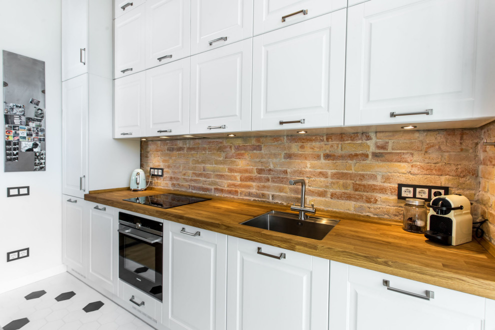 This is an example of a large industrial single-wall eat-in kitchen in Barcelona with a single-bowl sink, shaker cabinets, white cabinets, wood benchtops, grey splashback, metal splashback, white appliances, medium hardwood floors, with island, white floor, brown benchtop and vaulted.