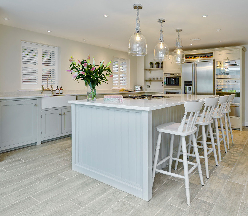 Photo of a medium sized classic l-shaped kitchen with a belfast sink, beaded cabinets, grey cabinets, stainless steel appliances, an island, grey floors and white worktops.