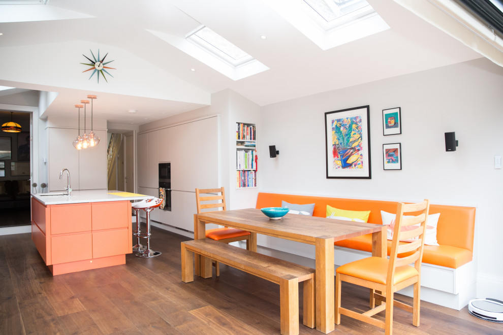 This is an example of a mid-sized modern u-shaped open plan kitchen in London with a single-bowl sink, flat-panel cabinets, orange cabinets, solid surface benchtops, orange splashback, glass tile splashback, dark hardwood floors, with island, brown floor and white benchtop.