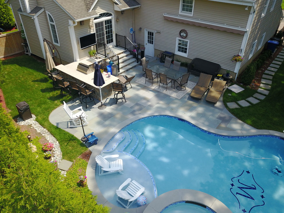 Photo of a mid-sized traditional backyard custom-shaped natural pool in New York with natural stone pavers.