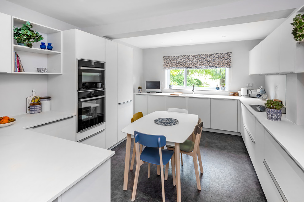 Design ideas for a mid-sized modern u-shaped eat-in kitchen in Other with a drop-in sink, blue splashback, stone tile splashback, black appliances, a peninsula, flat-panel cabinets, white cabinets, black floor and white benchtop.